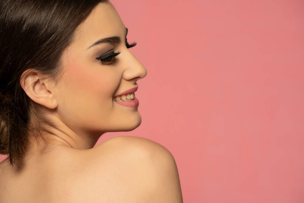 A beautiful smiling girl with smooth skin and make-up on a pink background. .fashion, beauty, makeup, cosmetics, beauty salon, style - Foto, imagen