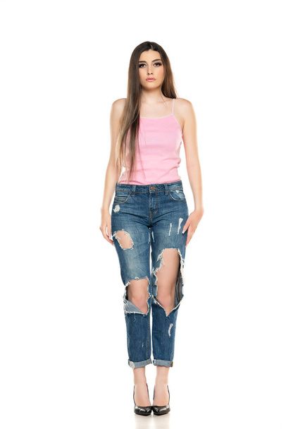 Приваблива молода жінка позує в рваних джинсах і літній сорочці. Модний погляд на білому тлі
 - Фото, зображення