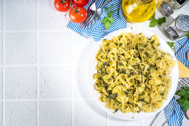 Italian mediterranean lunch concept. Farfalle pasta with spinach, mushrooms, vegetables and creamy sauce. On a white tile table, with spices for dinner copy space - Fotografie, Obrázek