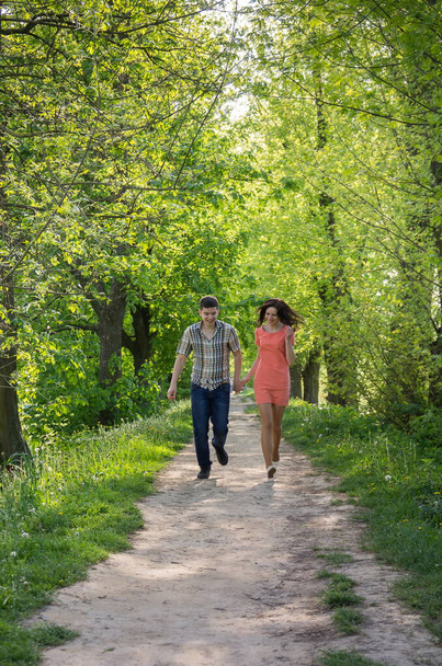 Una giovane coppia innamorata, un ragazzo e una ragazza, corrono lungo il vicolo del parco verso di loro. - Foto, immagini