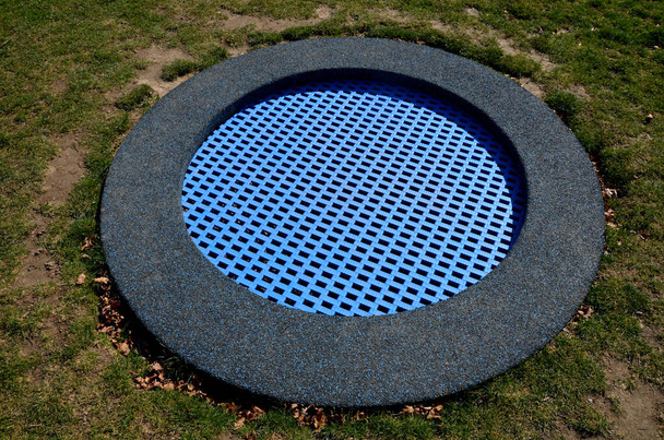 芝生と円形のトランポリンで遊び場の青いゴム製の表面が地形に沈んでいます。子供たちは家の裏にある公園でいくつかのトリックや. - 写真・画像