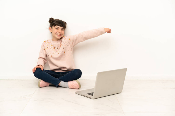 Little girl with a laptop sitting on the floor giving a thumbs up gesture - Photo, Image