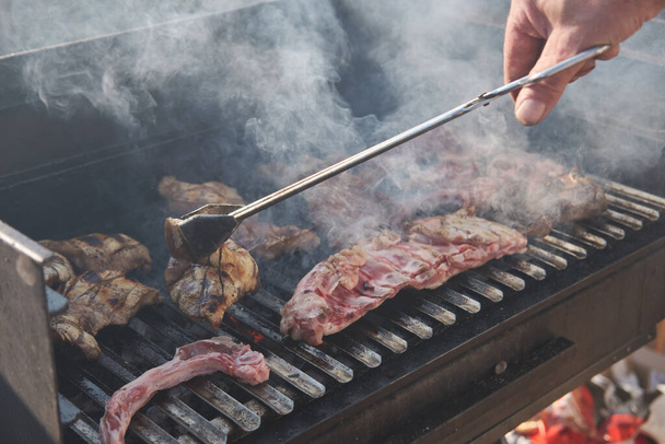 Een man koken ribbetjes op barbecue grill voor de zomer outdoor party. BBQ rook. Voedselachtergrond. - Foto, afbeelding