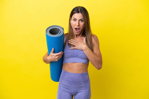 Sportlerin, die Yoga-Kurse besucht, während sie eine Matte hält, die nicht gelb ist, überrascht und schockiert, während sie nach rechts schaut - Foto, Bild
