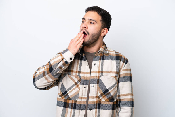 Jovem brasileiro isolado sobre fundo branco bocejando e cobrindo ampla boca aberta com a mão - Foto, Imagem