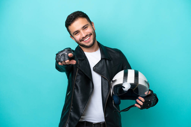 Молода бразилька з мотоциклетним шоломом, ізольована на синьому фоні, вказує спереду з радісним виразом. - Фото, зображення