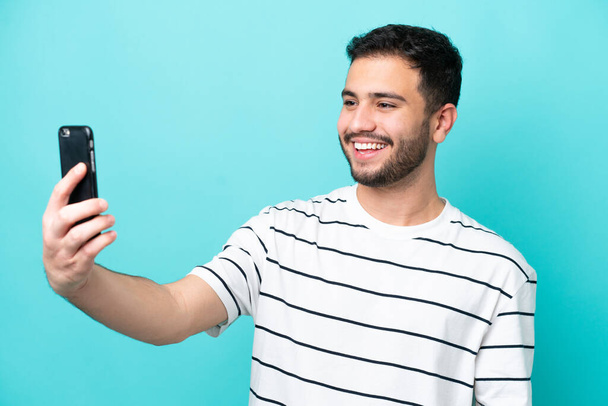 Young Brazilian man isolated on blue background making a selfie with mobile phone - Fotografie, Obrázek
