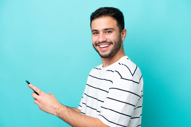 Young Brazilian man isolated on blue background sending a message or email with the mobile - Zdjęcie, obraz