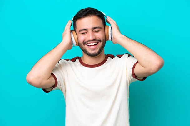 Fiatal brazil férfi elszigetelt kék háttér hallgat zenét - Fotó, kép