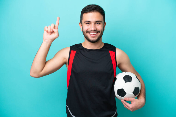 Jeune footballeur brésilien isolé sur fond bleu pointant vers le haut d'une excellente idée - Photo, image