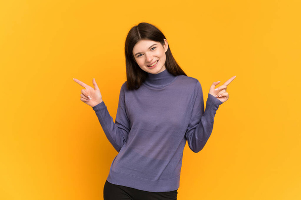 Young Ukrainian girl isolated on yellow background pointing finger to the laterals and happy - Photo, Image