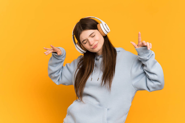 Giovane ragazza ucraina isolata su sfondo giallo ascoltare musica e ballare - Foto, immagini