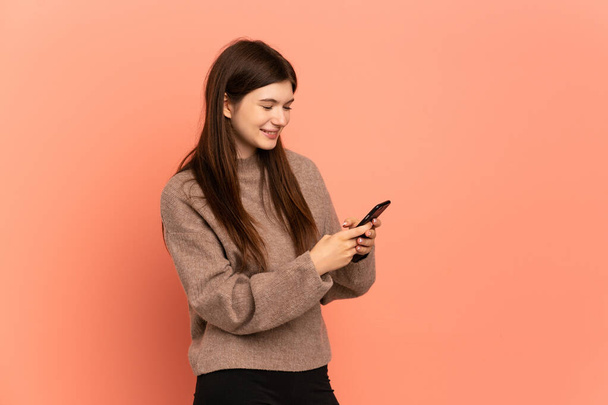 Joven ucraniana aislada sobre fondo rosa enviando un mensaje o correo electrónico con el móvil - Foto, imagen