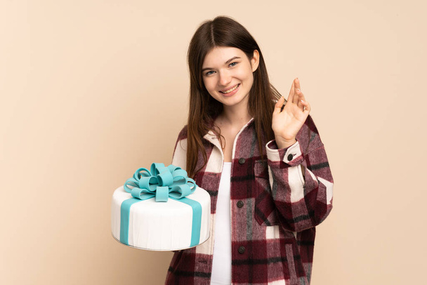 Young Ukrainian girl holding a big cake isolated on beige background saluting with hand with happy expression - Foto, Imagem