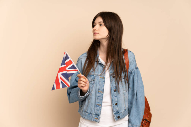 Junge Ukrainerin mit einer britischen Flagge auf beigem Hintergrund, die zur Seite schaut - Foto, Bild