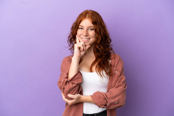 tiener roodharige meisje over geïsoleerde paarse achtergrond gelukkig en glimlachen - Foto, afbeelding