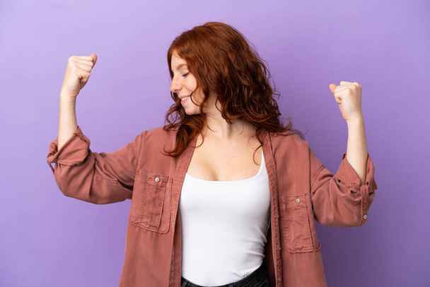 tiener roodharige meisje over geïsoleerde paarse achtergrond doen sterke gebaar - Foto, afbeelding