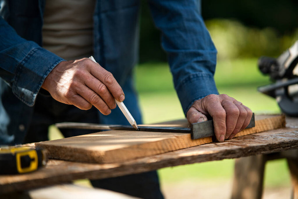 Close-up of handyman measuring a board, outside in garden. - Photo, Image