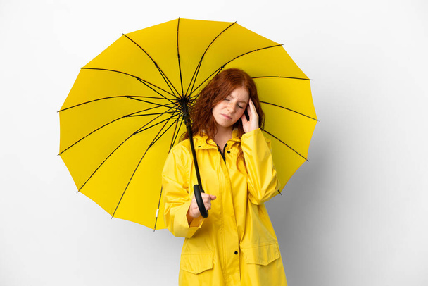 Adolescente ruiva menina capa impermeável e guarda-chuva isolado no fundo branco com dor de cabeça - Foto, Imagem