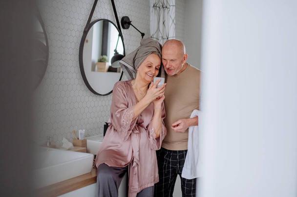 Senior couple in love in bathroom, using smartphone, morning routine concept. - Foto, afbeelding