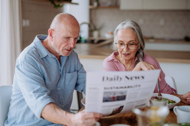 Happy senior couple having breakfast and reading newspaper together at home. - Fotografie, Obrázek