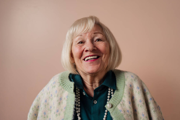 Smiling elegant elderly woman on pink color background, studio portrait - Foto, Imagen