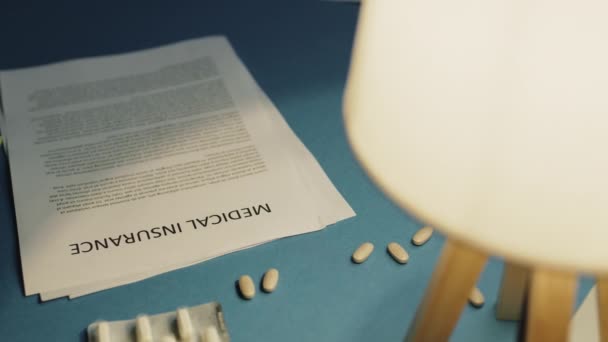 Orvosi biztosítási lap a kék íróasztalon lámpával - Felvétel, videó