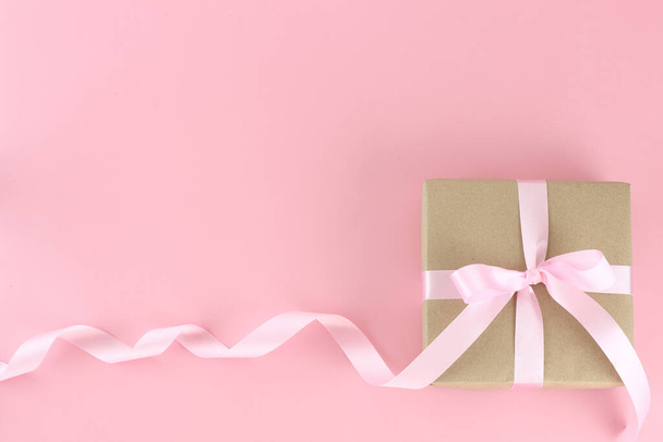 Top view brown paper gift box with pink satin curly ribbon bow on pastel pink background. Flat lay mother day, father day, valentines day, birthday concepts with copy space. - 写真・画像