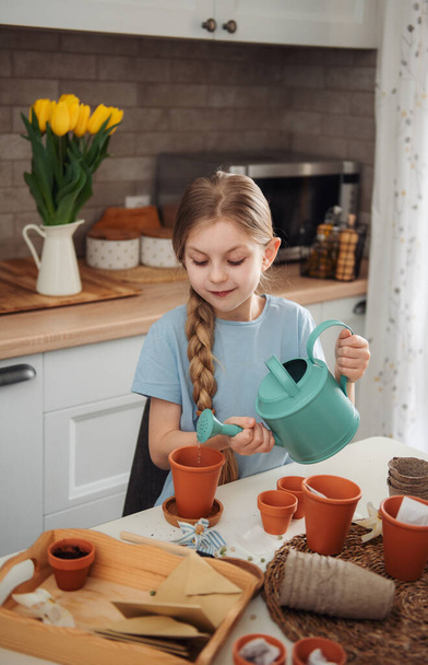 Little girl sitting at the table at home, sowing seeds into flower pots. Home gardening  - Foto, Bild