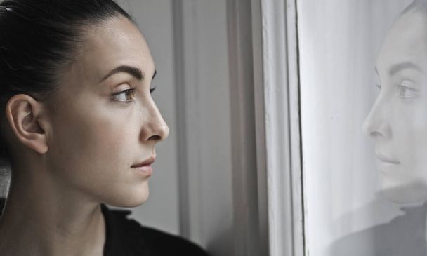 young woman looks out the window - Φωτογραφία, εικόνα