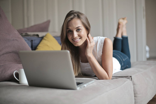 portrait of young woman lying on a sofa while working with a computer - Foto, imagen