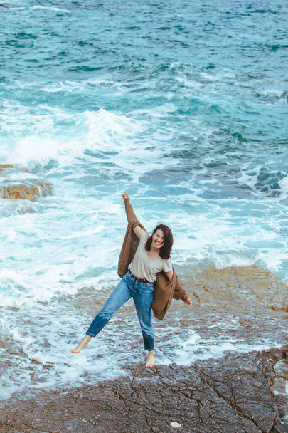 woman walking by rocky beach in wet jeans barefoot. summer sea vacation - Photo, Image