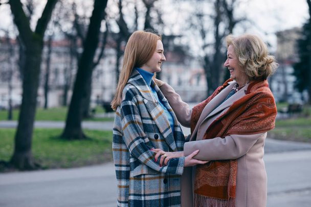 Een oma raakt het gezicht van haar tienerkleindochter met genegenheid aan. Ze ontmoetten elkaar in het park bij koud weer.. - Foto, afbeelding