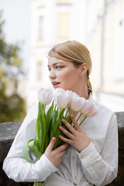 pretty woman looking away while holding white tulips outdoors - Fotografie, Obrázek