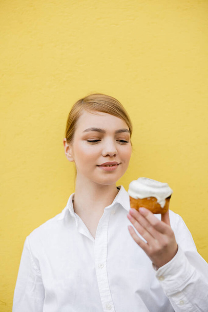 smiling woman looking at delicious cupcake isolated on yellow - Fotó, kép