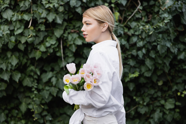side view of young woman with white tulips near green ivy outdoors - Foto, Bild