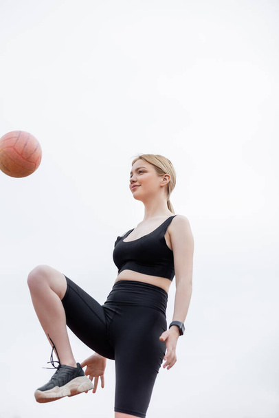 low angle view of smiling sportswoman training with ball outdoors - Photo, Image