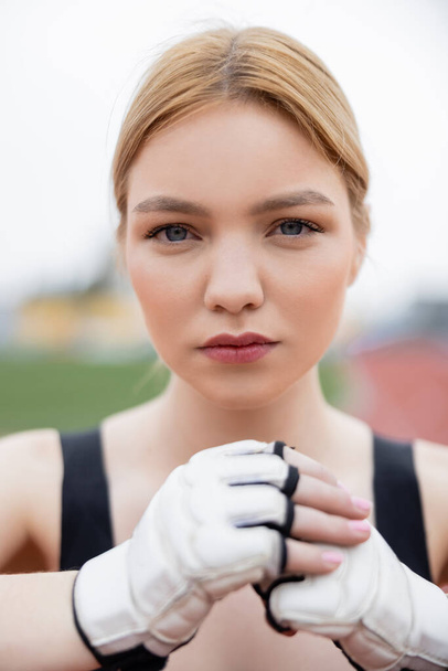 pretty young sportswoman in fitness gloves looking at camera outdoors - Φωτογραφία, εικόνα