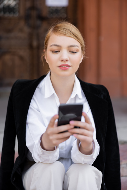 junge blonde Frau im weißen Hemd mit Handy im Freien - Foto, Bild
