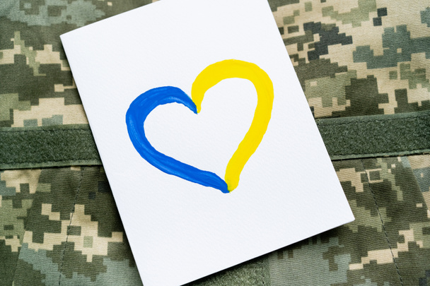 Κάτοψη κάρτας με μπλε και κίτρινη καρδούλα σε στρατιωτική στολή  - Φωτογραφία, εικόνα