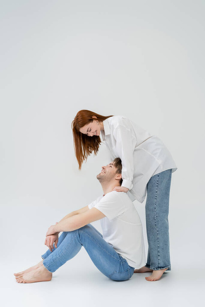 Cheerful woman in shirt looking at boyfriend on white background - Foto, imagen