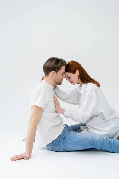 Side view of redhead woman with closed eyes touching chest of boyfriend on white background - Foto, Imagem