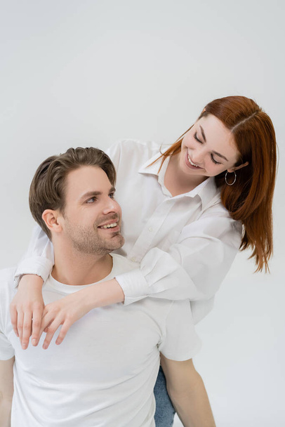 Redhead woman in shirt embracing positive boyfriend isolated on white  - Fotografie, Obrázek