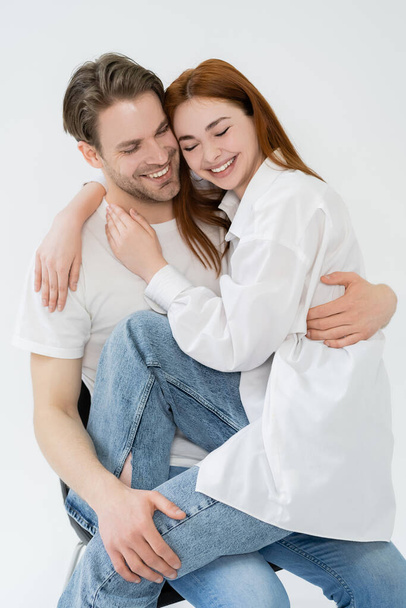 Positive couple hugging while sitting on chair isolated on white  - Fotografie, Obrázek