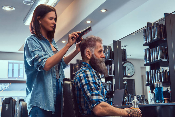 Woman hairdresser cutting hairs of old man hupster in barbershop - Foto, Bild