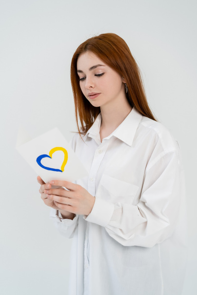 Rothaarige Frau im Hemd mit blauem und gelbem Herzschild auf weißem Hintergrund  - Foto, Bild