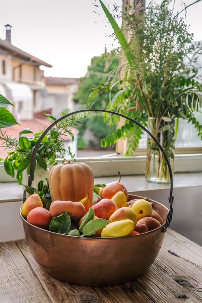 Meyve ve sebzeler büyük bir bakır kasede. Pencereden köy manzaralı. - Fotoğraf, Görsel