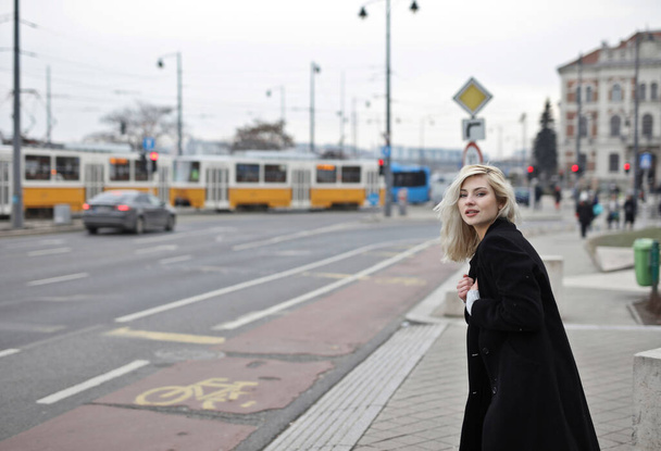 portrait of young woman in a black coat in the street - Фото, изображение