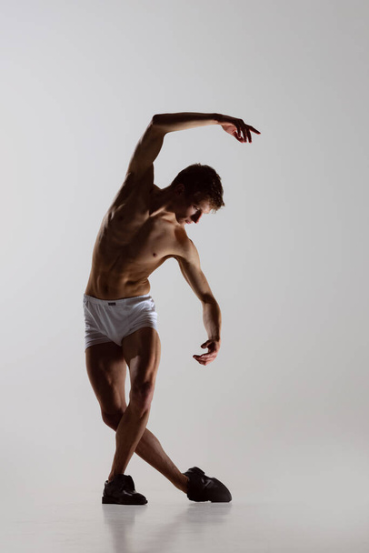 Contemp dance, performance. Young flexible shirtless man in underwear dancing isolated on gray background. Art, music, beauty. Healthy lifestyle concept - 写真・画像
