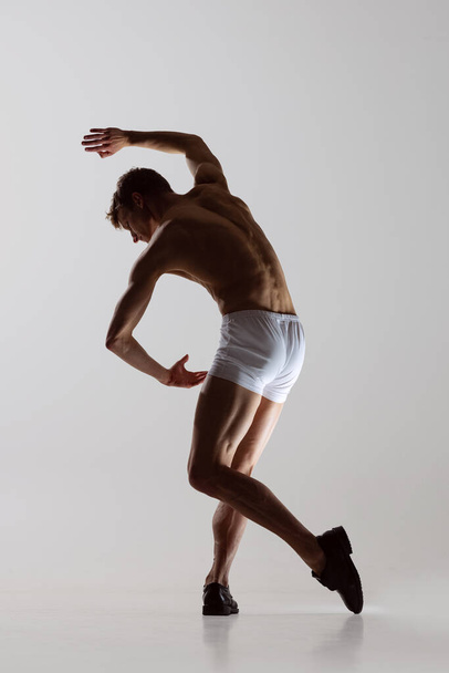 Contemp dance, performance. Young flexible shirtless man in underwear dancing isolated on gray background. Art, music, beauty. Healthy lifestyle concept - Valokuva, kuva